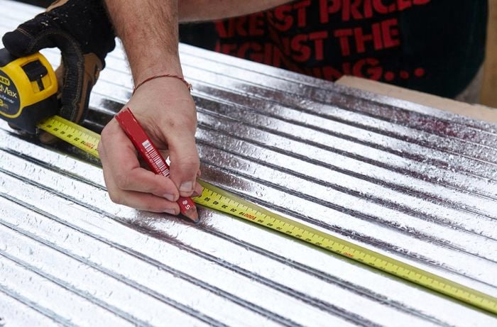 Corrugated iron being measured and marked for cutting with a pencil and tape measure