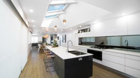 Long kitchen painted white with island bench and angled ceiling with multiple skylights