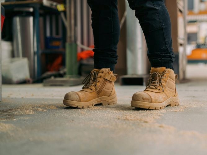A person with work boots on standing in a construction site.