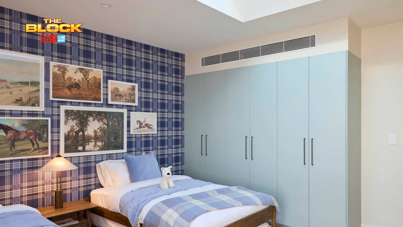 Blue bedroom with a check wallpapered wall and twin beds with blue linens. Above the beds are various horse artworks arranged sporadically and a plae blue wardrobe on the opposite wall.