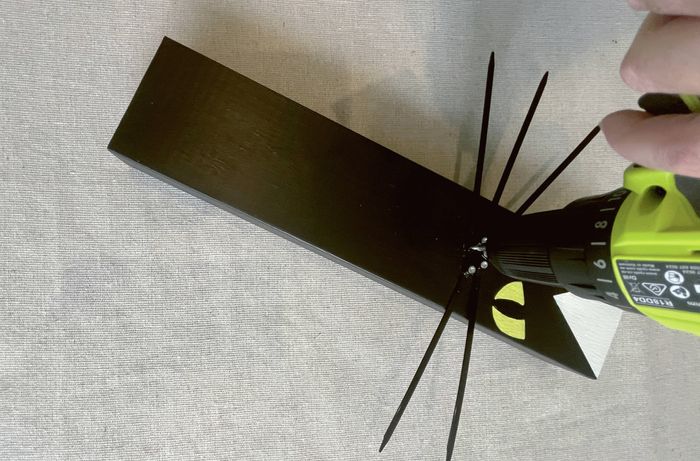 A hand using a drill to screw into a black wooden cat decoration with yellow eyes and black whiskers.