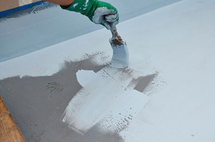 A person applying waterproofing to a bathroom floor with a brush