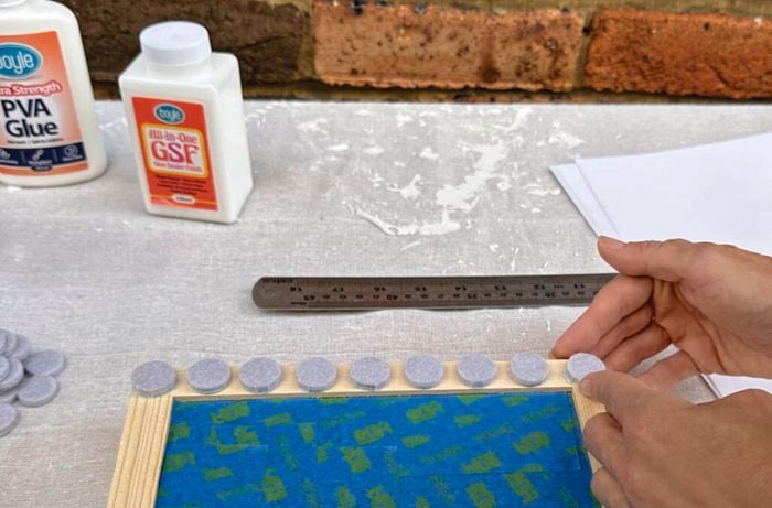 Hands sticking felt floor protectors on a wooden picture frame