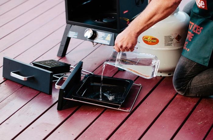 Person adding water to a vertical smoker tray