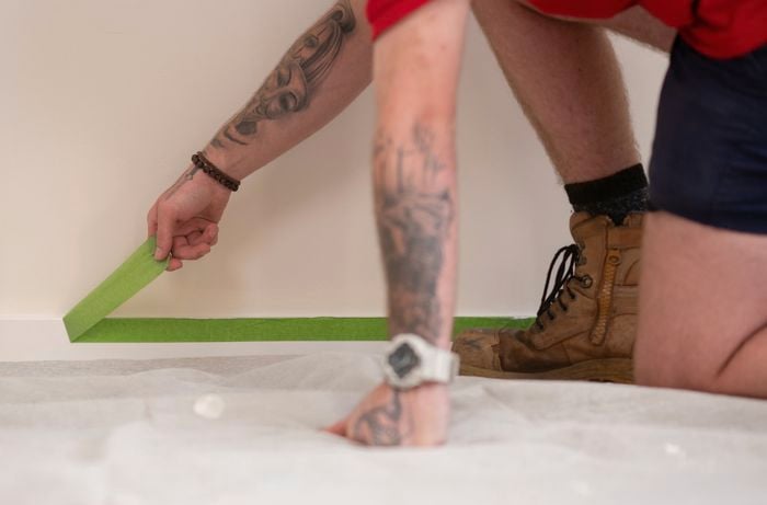 A person adorned with a hand tattoo and wearing a beaded bracelet is peeling off painter's tape.