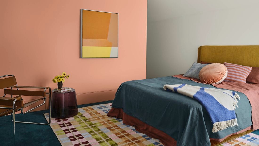A stylised bedroom with a feature wall painted in Dulux’s baked clay, a bed and rug in on-trend colours.]