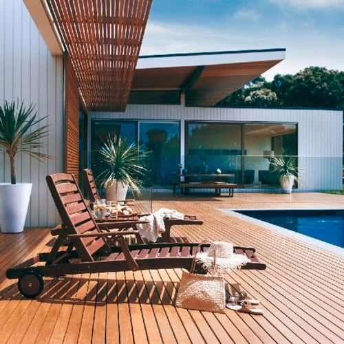 Outdoor decking area and lounge timber chairs alongside a pool and potted yuccas