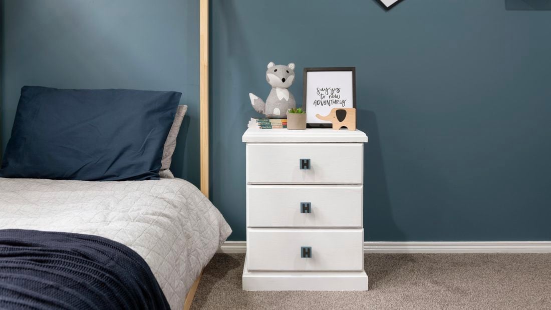 A white chest of drawers with handles customised with the letter H, in a blue themed bedroom setting