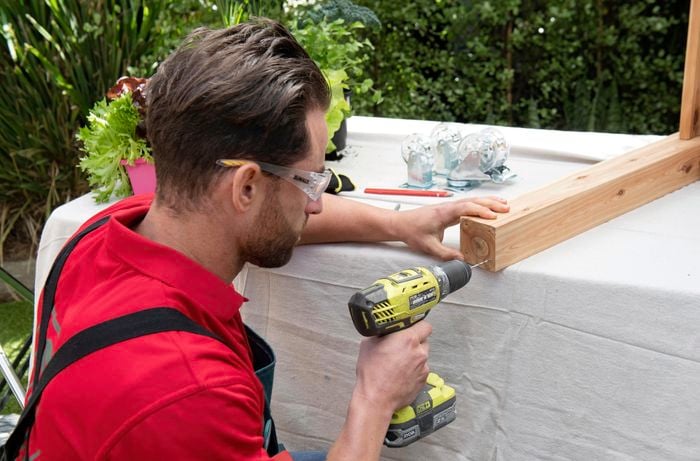 A person drilling a hole in  the end of a piece of timber