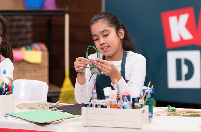 A young girl is using a pipe cleaner to make a loop at the top of her popsicle character.