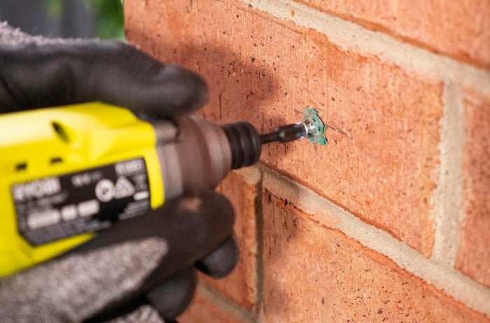 Person drilling screws into brick wall and plug.