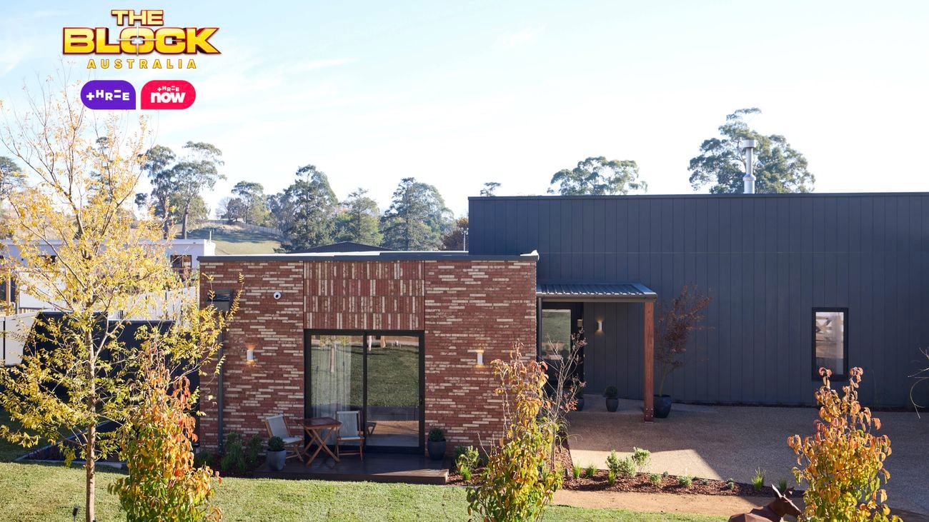 A front area of a house with trees, paving, shrubs and a grass area in it.