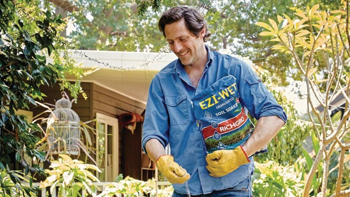Man in yellow gloves sprinkles seeds on garden