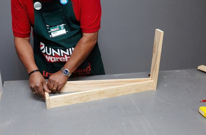 A person fitting a bottom piece of timber to A-frame legs