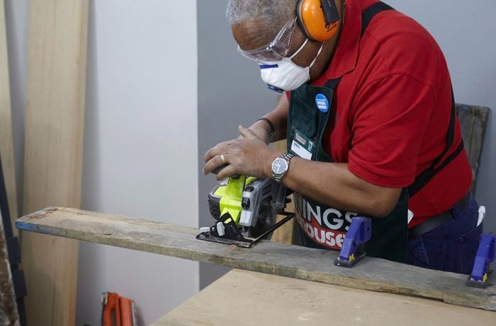 A person wearing protective gear cutting a length of timber using a circular saw