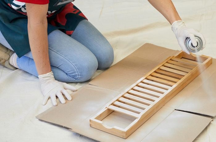 A woman sprays a timber bath caddy.