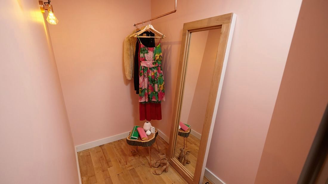 A narrow dressing room with a copper pipe clothes rack and full-length mirror in a timber frame