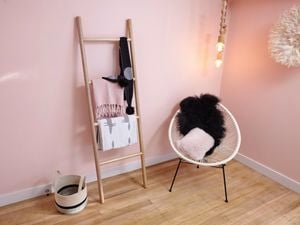 A wooden towel ladder with scarves leaning against a pink painted wall