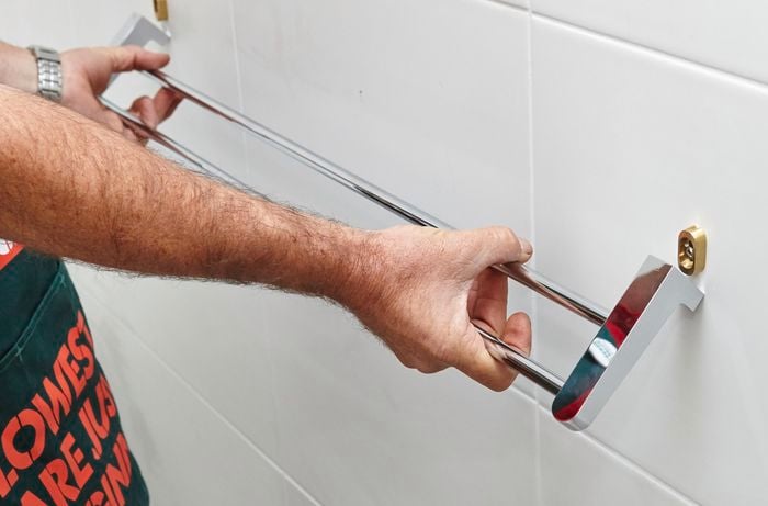 A person attaching a towel rail onto fittings attached to a tile wall