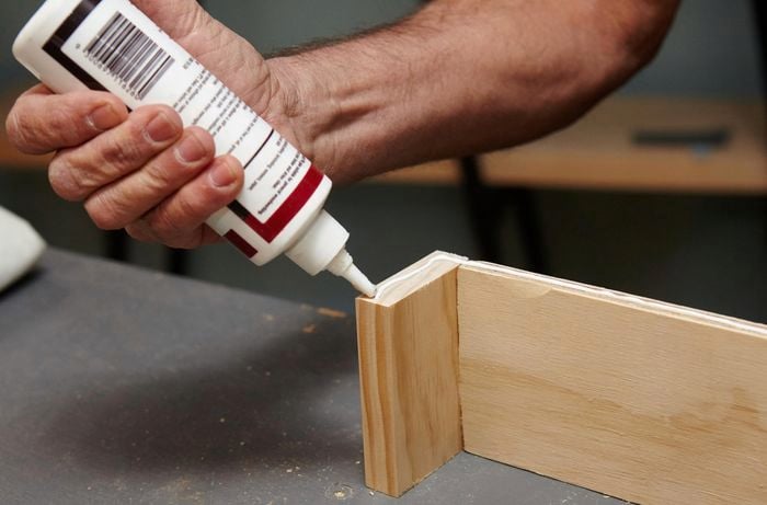A person applying glue to L-shaped pieces of timber