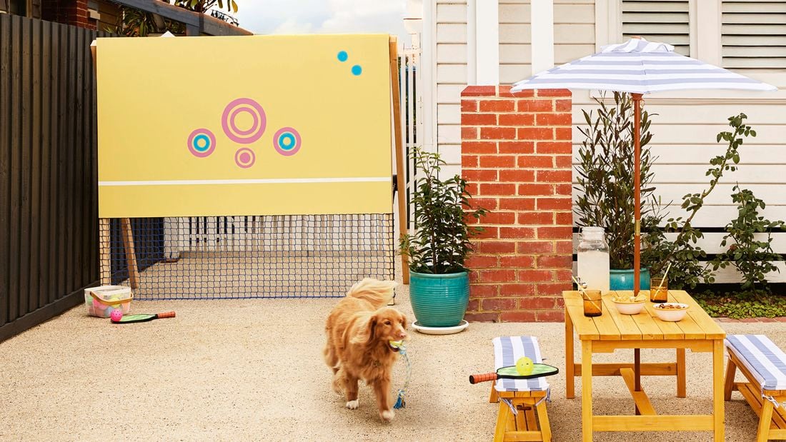 A yellow pickleball practice wall with colourful target circles and a blue net, set up outdoors.