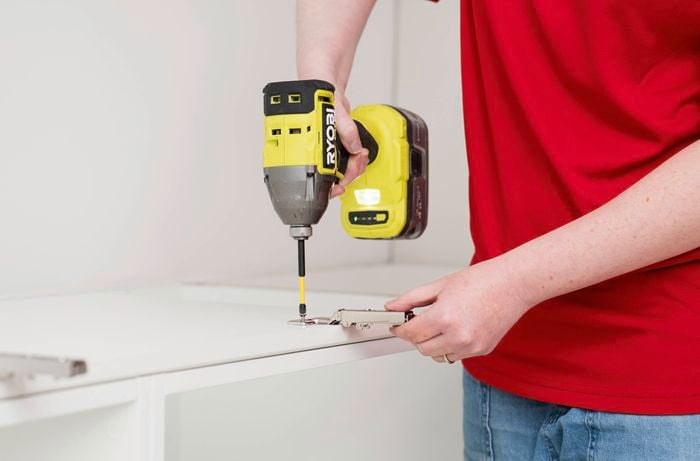 : A person is using a power drill to install the mounting plate to the inside of a cabinet frame.  