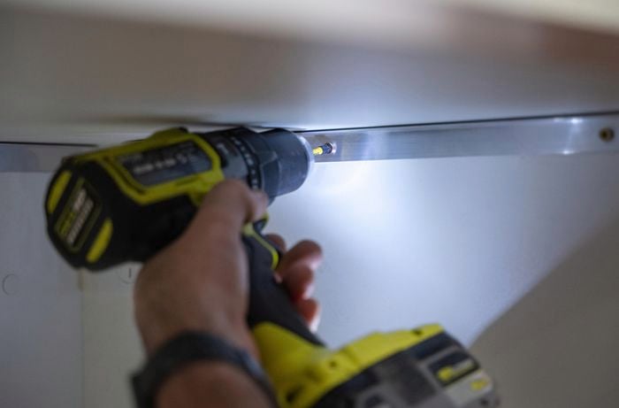 A person using power screwdriver to attach aluminium angles.