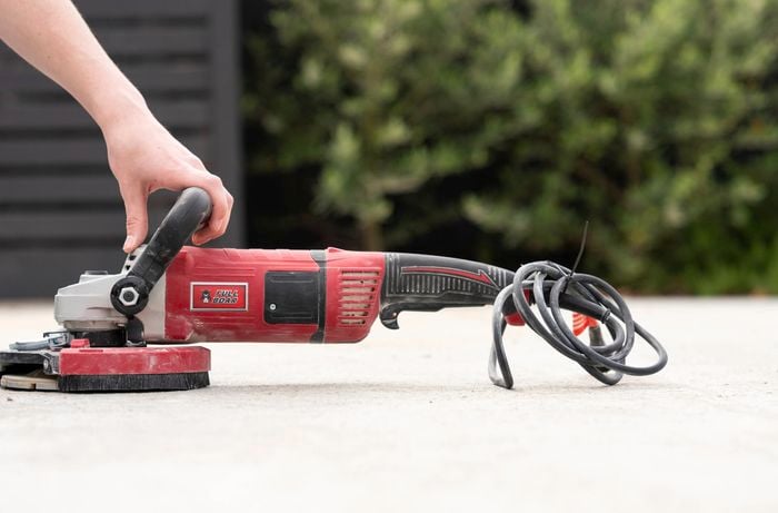 A person is using a concrete grinder on a concrete surface to remove previous concrete sealer or paint.