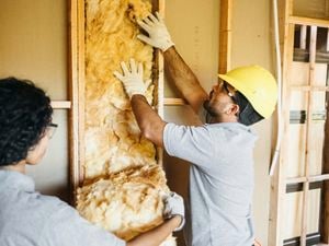 Construction workers fitting insulation in frame.