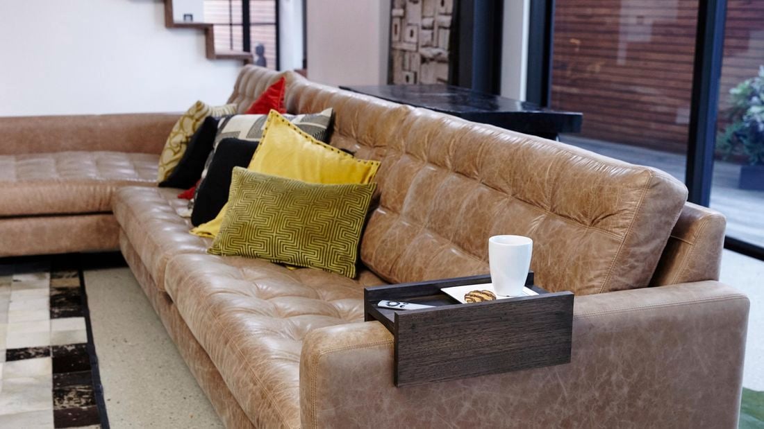 Wooden sofa arm table sitting on the arm of a brown leather couch