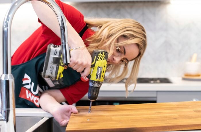 A Bunnings team member drilling holes into a cheese platter board for handles to be added