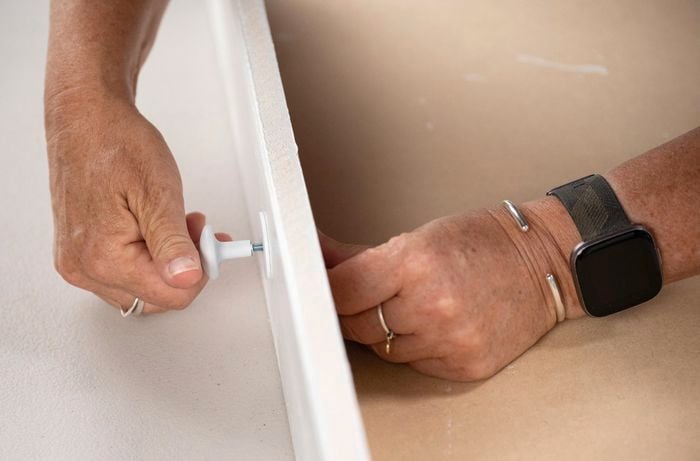 A person holding a drawer knob next to a piece of wood