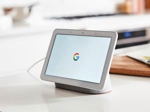 A google tablet sitting in a charger in front of a chopping board in a white themed kitchen