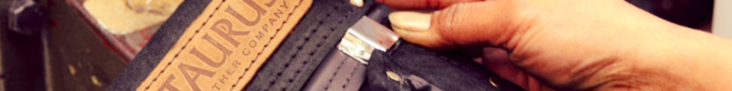 Hands crafting a leather sheath with a “TAURUS” label being stitched.