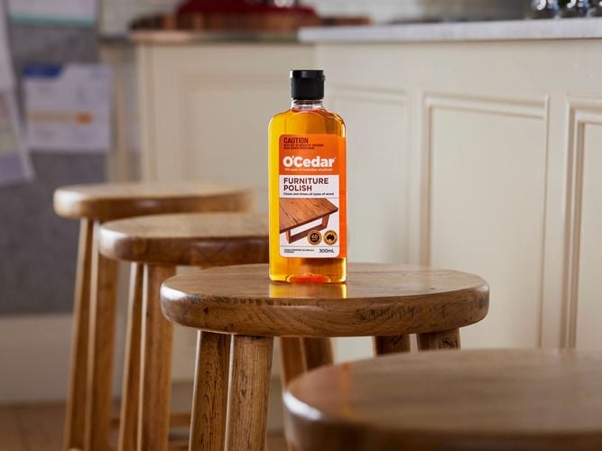 A bottle of O'Cedar Furniture Polish sitting on a wooden kitchen stool.