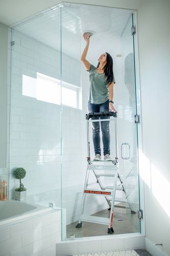 Woman on step ladder changing light globe in shower