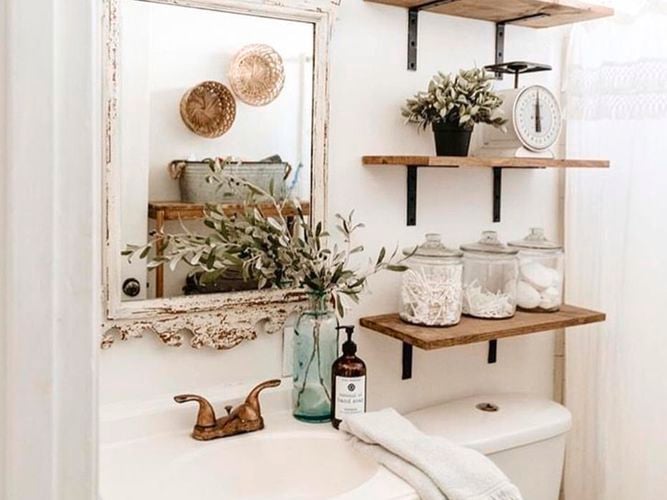 A bathroom with a basin, toilet, mirror and shelving on the wall in it