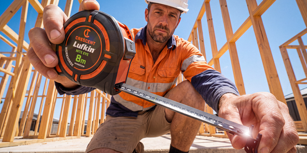 Worker measuring a timber frame with a Crescent Lufkin 8m tape measure on a construction site.