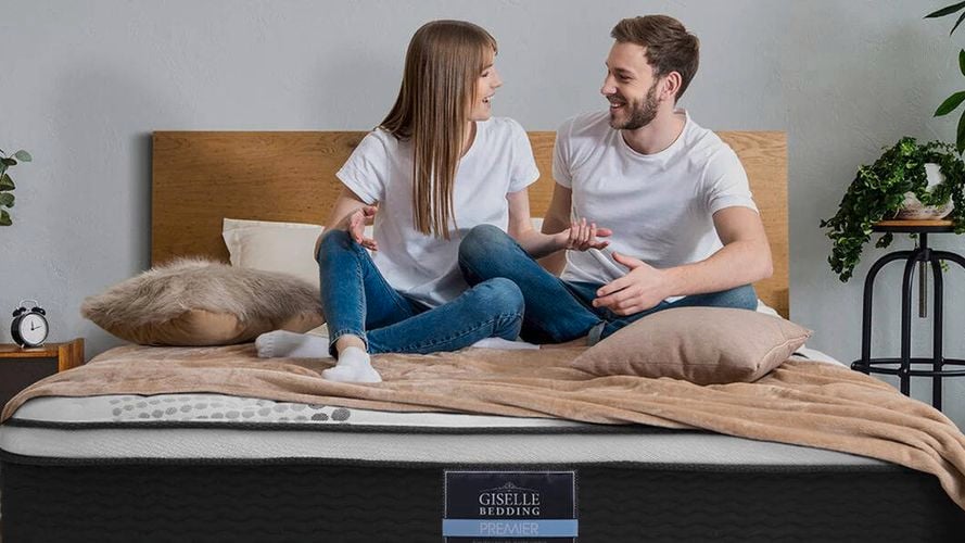 Two people sitting on a Giselle Bedding mattress in a cozy bedroom.