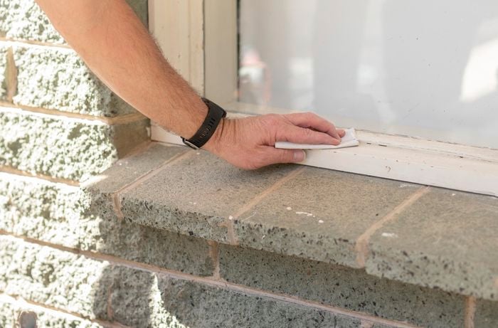 A persons hand prepares the window frame by sanding back the window frame to remove any existing paint.
