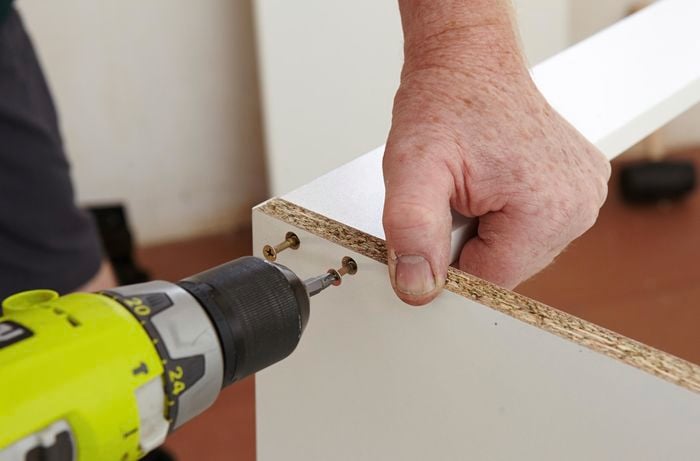 Person using a cordless driver to attach two cabinet panels
