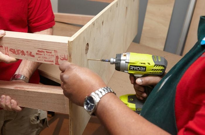 Person drilling timber legs onto ply panel