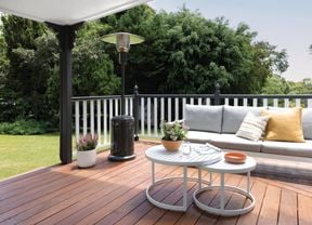 Outdoor entertaining area with wooden deck, grey and white lounge and coffee table, and an outdoor heater.