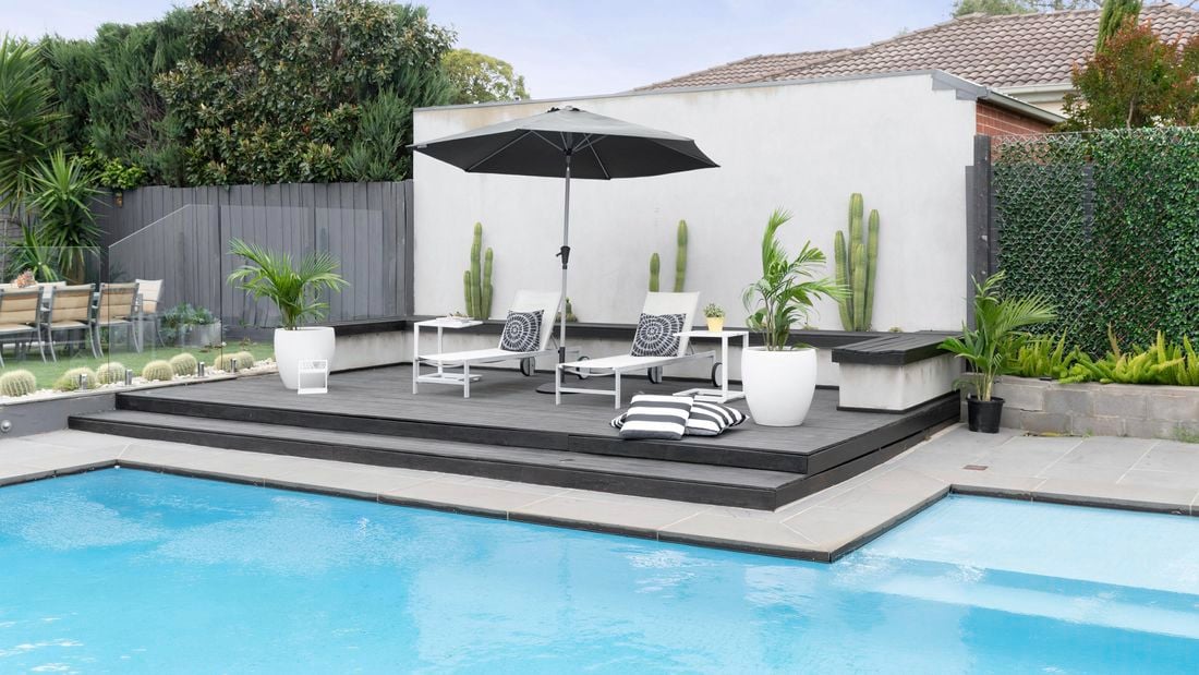 A wide shot of an outdoor pool area, with umbrella, sunbeds and throw cushions