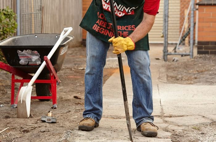 Bunnings team member using a fencing bar to pry concrete from the ground