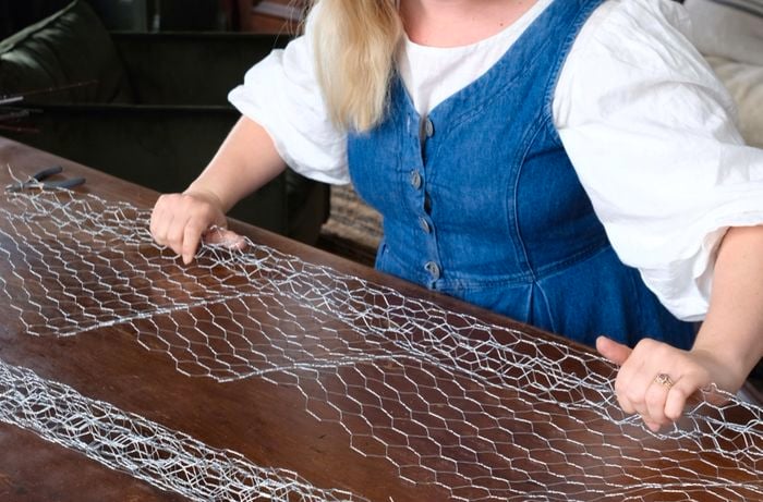 Lady rolling a long piece of wire netting, with a completed roll in front of her.
