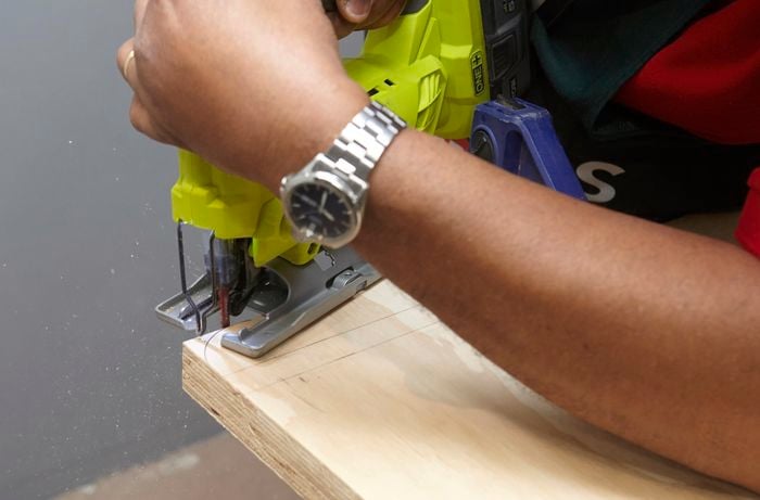 Person using jigsaw to cut a curved edge on a rectangular piece of ply wood.