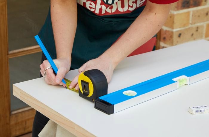 A person marks a measurement on a door. A pencil, measuring tape, level and rubber are shown.