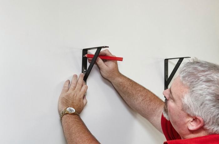 A person marking the holes for a bracket on a wall