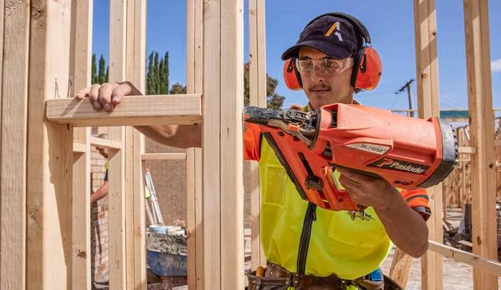 A tradie uses a Paslode nail gun on a frame wearing hearing protection